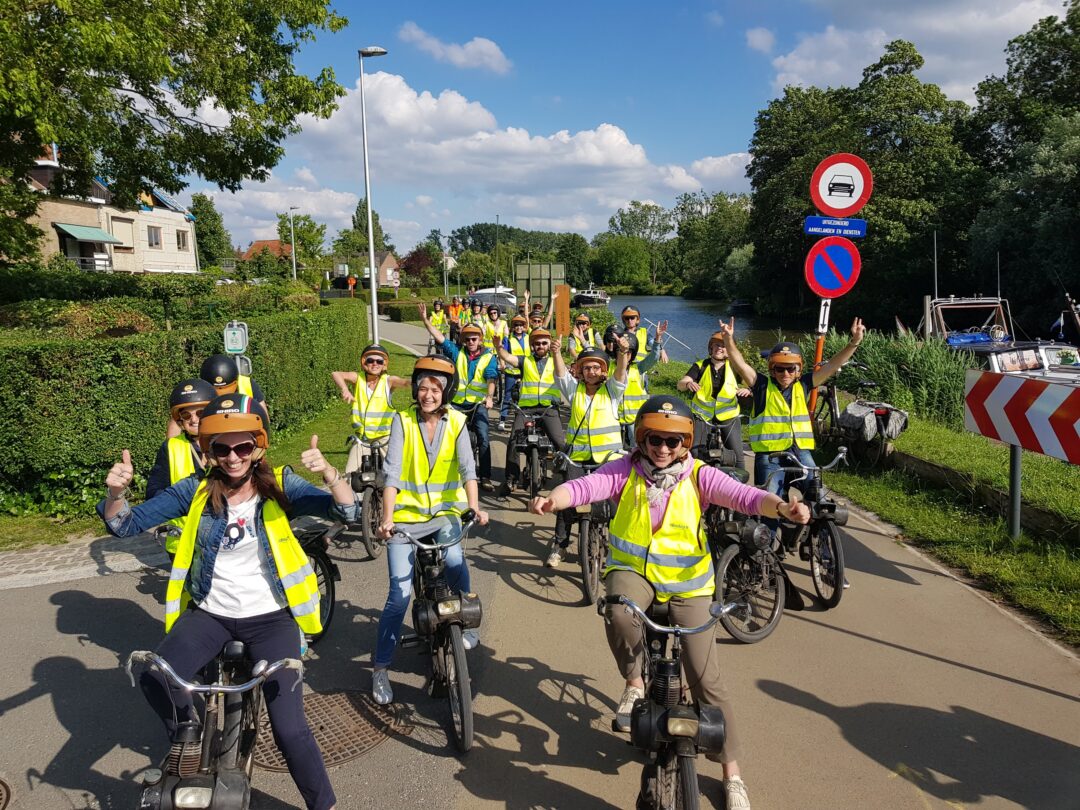 Groep deelnemers op Solex tijdens een teambuilding in Brugge, langs de Brugse Reien